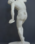 Photo with gray background of plaster cast sculpture of male faun or satyr from the back dancing with instruments attached to his hands