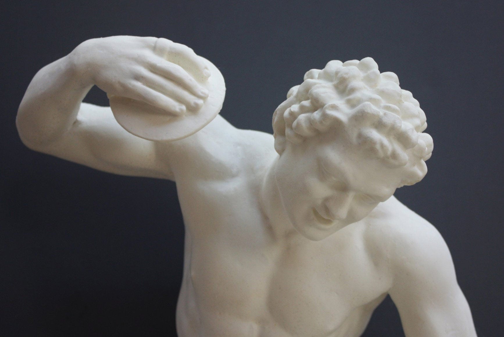 Photo closeup with gray background of plaster cast sculpture of male faun or satyr dancing with instrument attached to his right hand