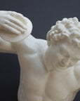 Photo closeup with gray background of plaster cast sculpture of male faun or satyr dancing with instrument attached to his right hand