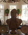 photo of plaster cast of male bust sculpture, namely Lafayette, in uniform on a table with decorative dishes and other furniture, dishes, plants, and bay windows behind