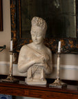 photo of plaster cast sculpture bust of Madame Recamier with high up-do and ribbon over forehead and hands crossed over chest covered in cloth on a dark wood table with bronze decorations, candlesticks, and bronze framed mirror and two pictures