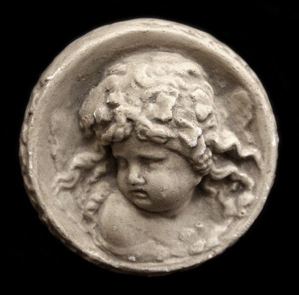 Photo of small round plaster sculpture medallion of head of an infant on a black background