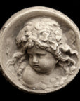 Photo of small round plaster sculpture medallion of head of an infant on a black background