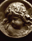 Photo of small round plaster sculpture medallion of head of an infant on a black background