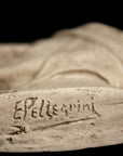 photo of plaster cast of small medallion with male portrait, view of bottom edge with artist signature on black background