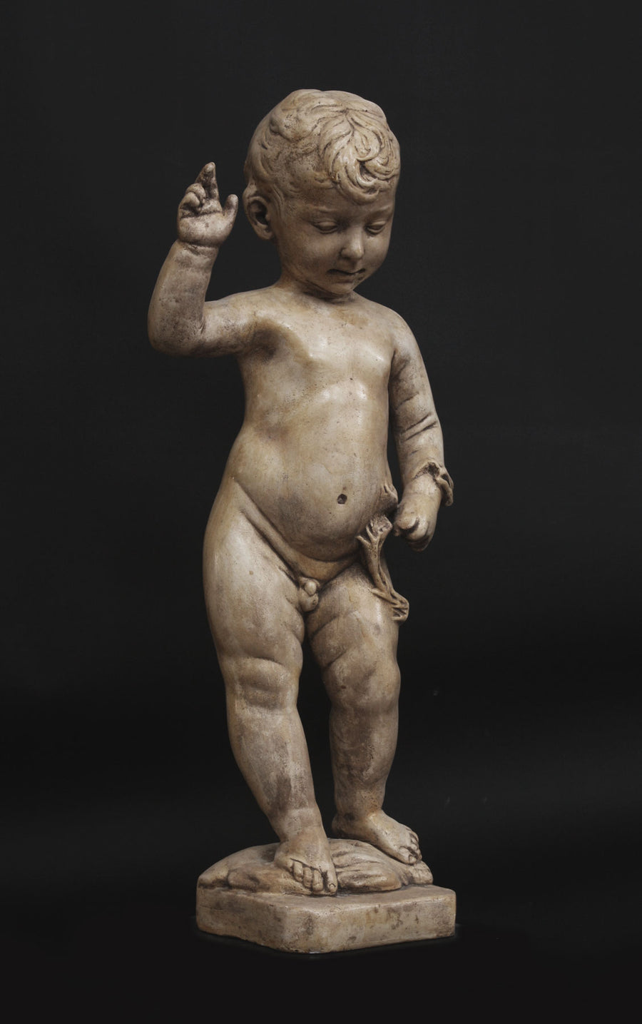 photo of plaster cast sculpture of nude male child, namely Christ, with raised right arm on a black background