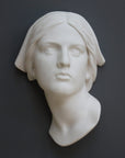 photo with gray background of plaster cast sculpture of Joan of Arc's face and portion of kerchief on head