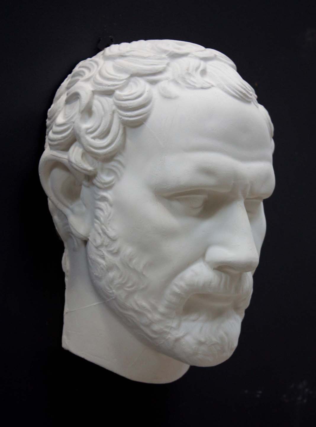 photo of white plaster cast of sculpture of face of Demosthenes with curly hair and beard on black background