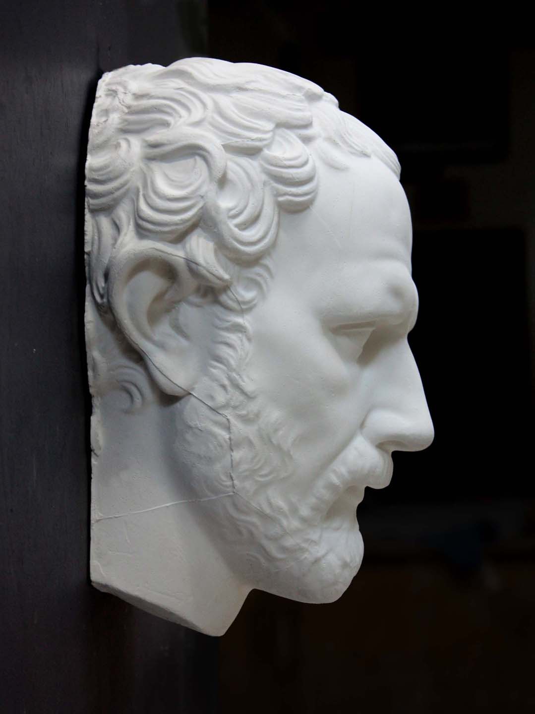 photo of white plaster cast of sculpture of face of Demosthenes with curly hair and beard on black background