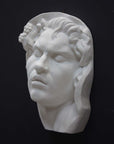 photo of plaster cast of sculpture of face of Sleeping Faun with two flowers in curly hair on dark gray background