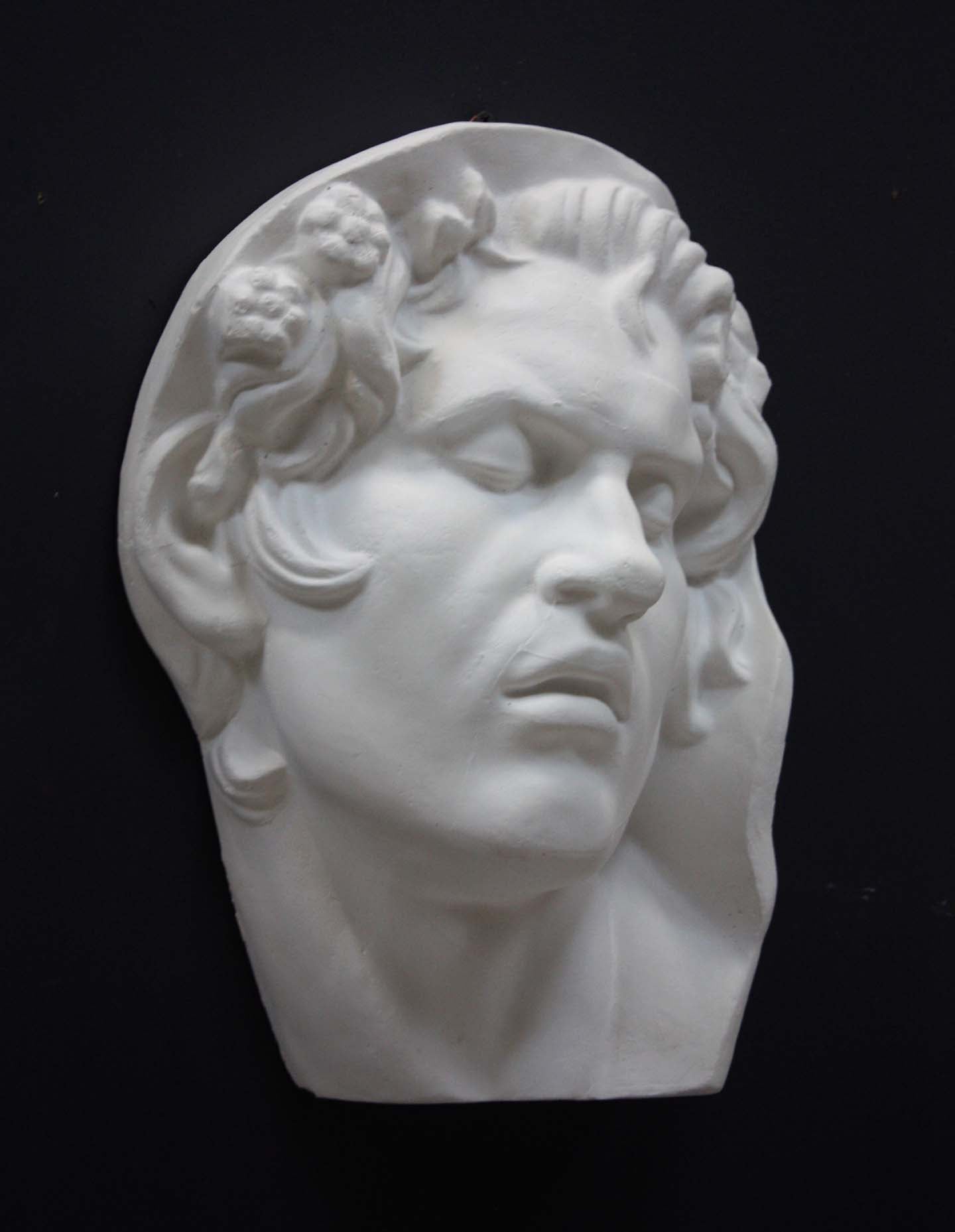 photo of plaster cast of sculpture of face of Sleeping Faun with two flowers in curly hair on dark gray background