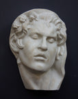 photo of plaster cast of sculpture of face of Sleeping Faun with two flowers in curly hair on dark gray background