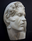 photo of plaster cast of sculpture of face of Sleeping Faun with two flowers in curly hair on dark gray background