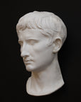 photo of white plaster cast sculpture of front half of head and neck of a male, namely Augustus Caesar, on black background