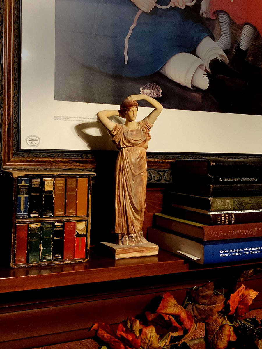 https://www.capronicollection.com/cdn/shop/products/318-Tanagra-Figurine-Arranging-Hair-on-dark-wood-mantel-beside-stack-of-books-and-miniature-books-with-art-print-behind_900x.jpg?v=1681495054