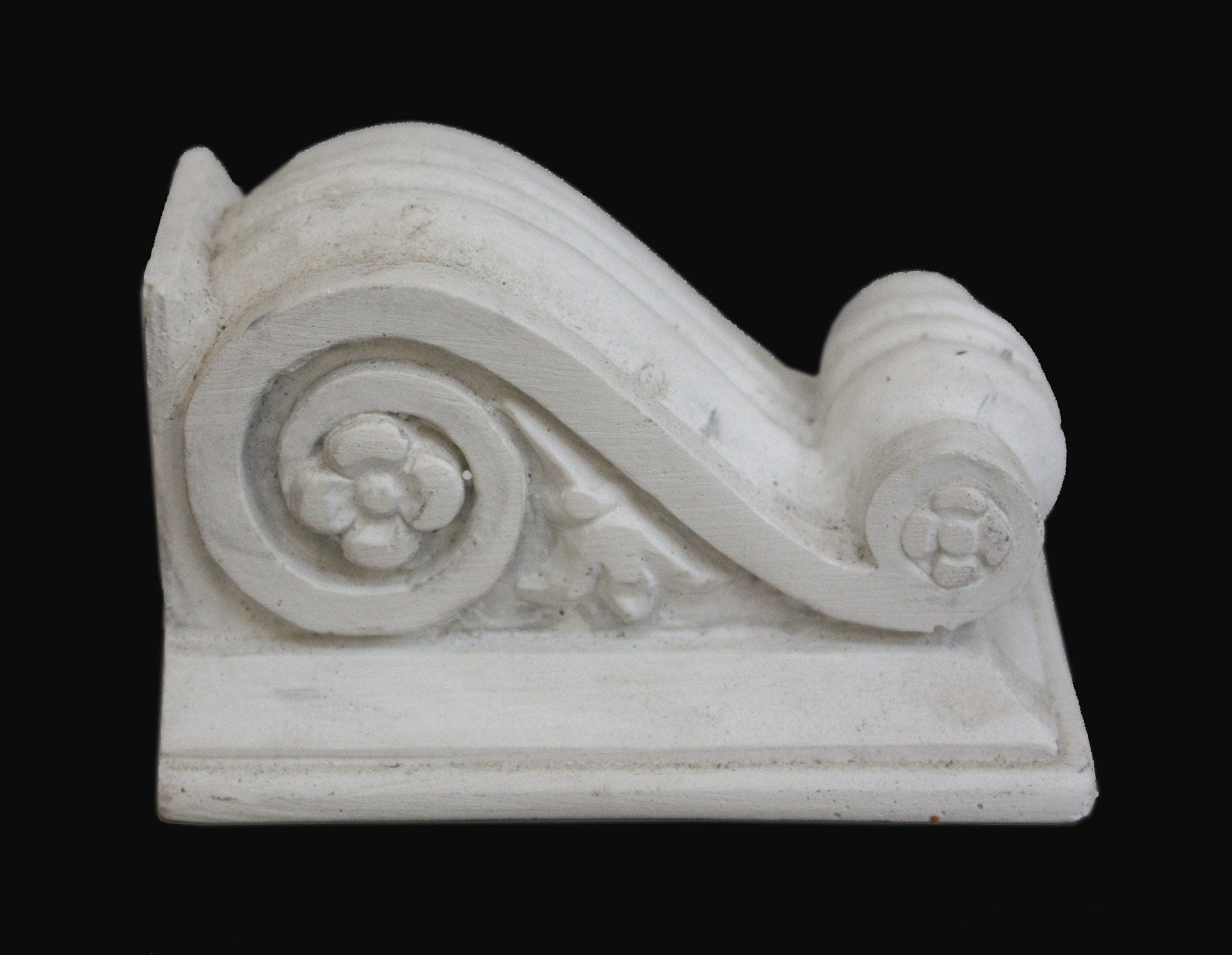 photo with black background of plaster cast of architectural bracket with scroll design