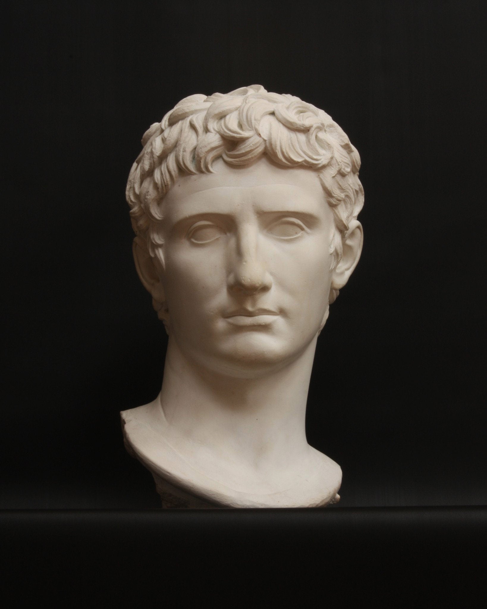 photo with black background of plaster cast of sculpted male bust, namely Augustus Caesar