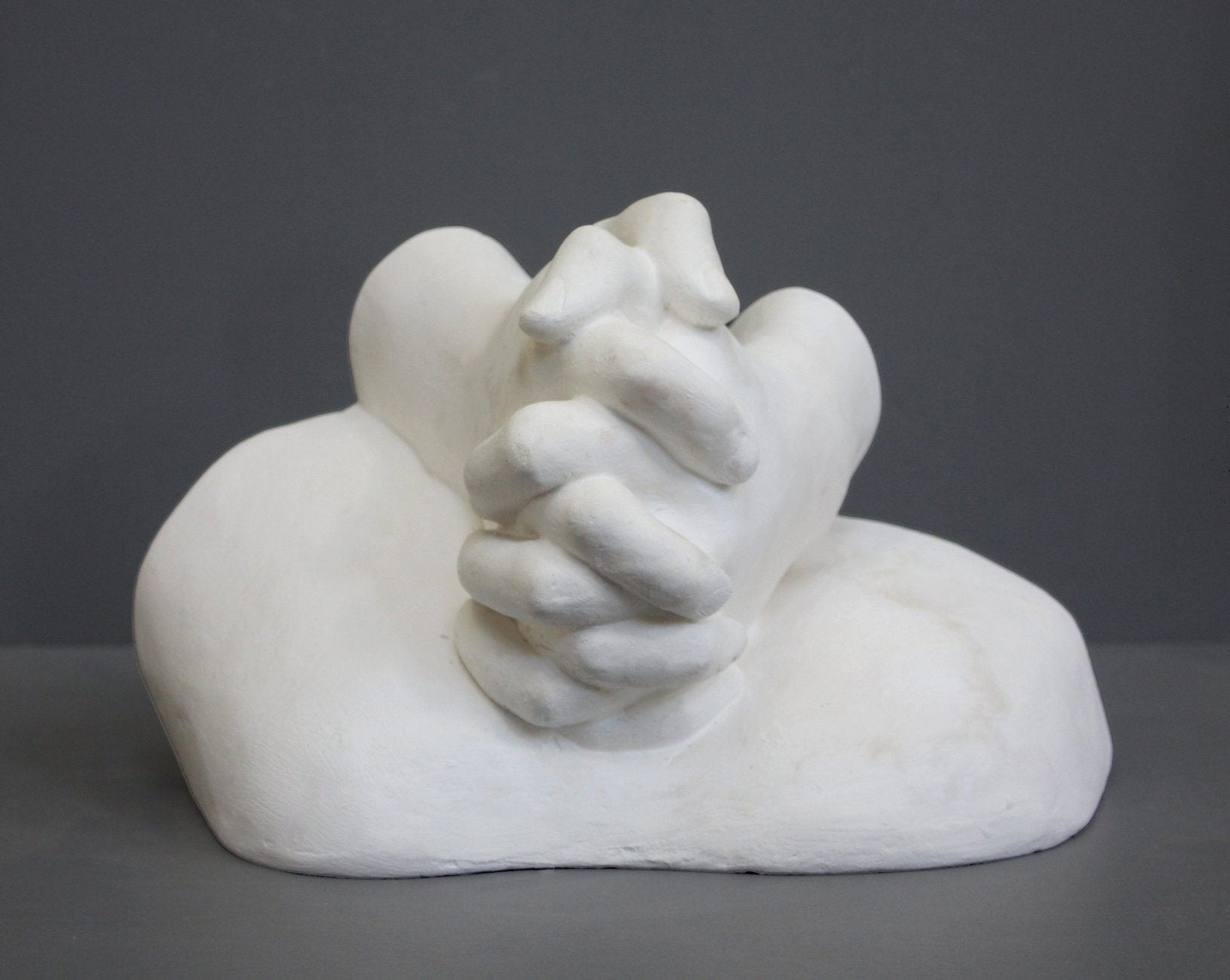 photo on gray background of plaster cast sculpture of Joan of Arc's hands clasped on top of a portion of her knees