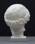 photo of plaster cast of sculpture of an Amazon head- female with pulled-back wavy hair on dark gray background