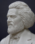 photo detail of white plaster cast sculpture of bust of Frederick Douglass with beard and in suit coat with toga over one shoulder on dark gray background