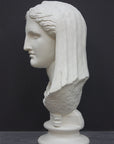 photo of white plaster cast of ancient sculpture of female head with curls and wrap, namely Demeter, on socle base on dark gray background