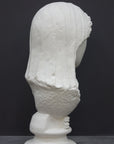 back view photo of white plaster cast of ancient sculpture of female head with curls and wrap, namely Demeter, on socle base on dark gray background