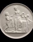 photo of off-white plaster cast relief sculpture of mostly nude female figure with two children and flowers and wreaths against black background