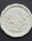 photo of white plaster cast relief sculpture of a child dancing and a female figure playing an instrument against dark gray background