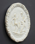 photo of white plaster cast relief sculpture of a child dancing and a female figure playing an instrument against dark gray background