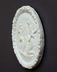 photo of white plaster cast relief sculpture of a child dancing and a female figure playing an instrument against dark gray background