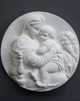 photo of relief plaster cast featuring the Madonna, Child, and St. John and hanging on a dark-colored wall