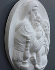 three-quarter photo of relief plaster cast featuring the Madonna, Child, and St. John and hanging on a dark-colored wall