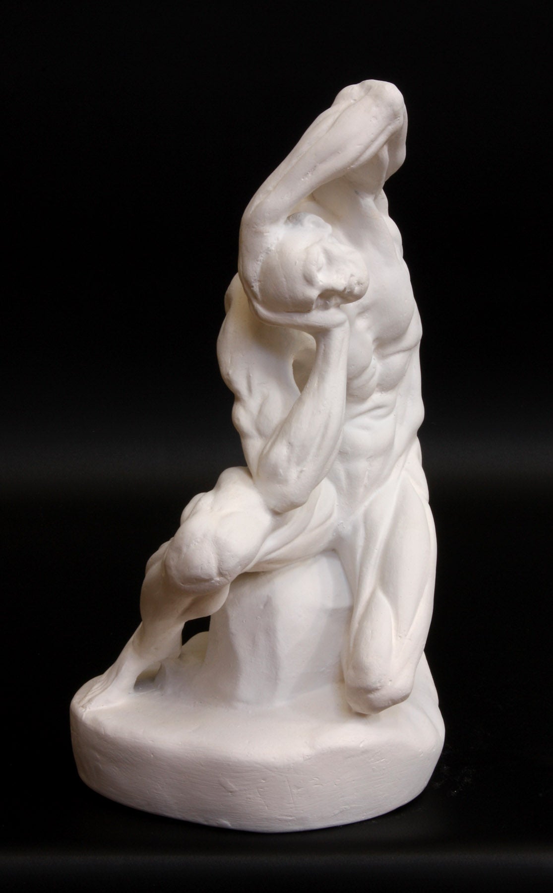 Photo of plaster cast sculpture of flayed man kneeling with hands on head on black background