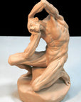 Photo of terracotta-colored plaster cast sculpture of flayed man kneeling with hands on head on white surface with black backdrop