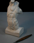 Photo of plaster cast sculpture of flayed male torso and a sculpting tool on a gray surface in front of a black background