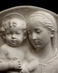 photo of plaster cast sculpture relief of the Madonna holding baby Jesus and angels in the background on a black background