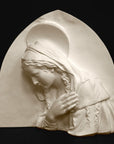 photo of plaster cast sculpture relief of the Madonna leaning over with her right hand crossed over her chest and a halo above her head on a black background