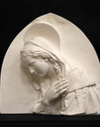 photo of plaster cast sculpture relief of the Madonna leaning over with her right hand crossed over her chest and a halo above her head on a black background