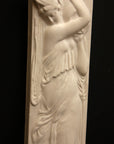 photo of plaster cast relief sculpture of female in drapery carrying jug over shoulder against black background