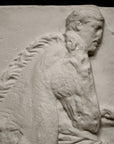 closeup photo of off-white plaster cast relief sculpture of three men on horseback from Parthenon against black background