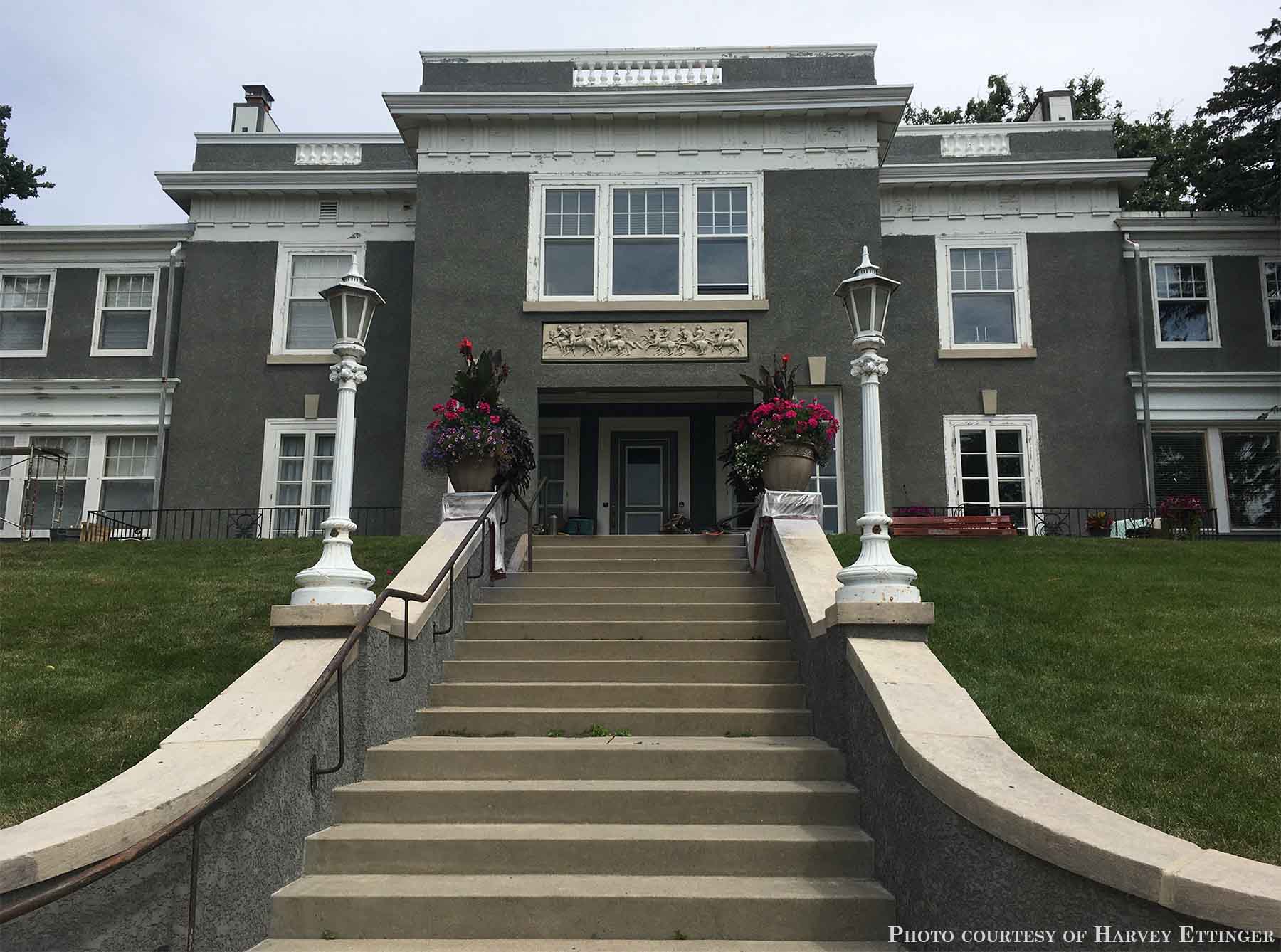 photo of plaster cast relief sculptures of men on horses above doorway on facade of gray house at the top of long staircase