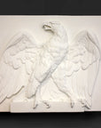 photo of white plaster cast of relief sculpture of an eagle calling, with its head turned toward the right and its wings open on gray background