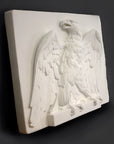 side photo of white plaster cast of relief sculpture of an eagle calling, with its head turned toward the right and its wings open on gray background