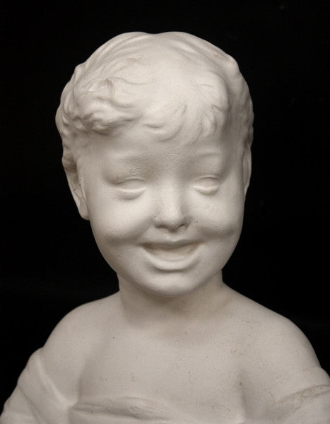 photo of white plaster cast sculpture bust of boy with open mouth, laughing, short hair, and clothes below his shoulders against a black background