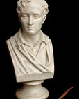 photo of white plaster cast sculpture bust of man, namely the poet Lord Byron, on socle base and sculpting tool beside it on black background