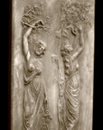 photo with black background of yellowed plaster cast relief sculpture of two robed female figures touching tree branches above their heads