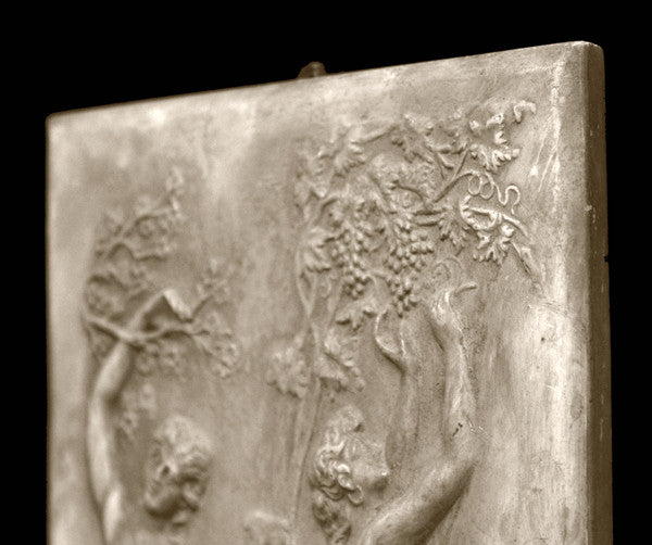 photo with black background of yellowed plaster cast relief sculpture of two robed female figures touching tree branches above their heads