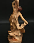 photo with black background of plaster cast sculpture from the back of female dancing with one arm raised and one arm lowered, holding onto drapery