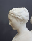 closeup photo of female head in profile from white plaster cast sculpture of three robed females standing in a circle with their backs to each other against a gray background