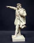 photo of plaster cast sculpture of standing man, namely Christopher Columbus, in robes and hat, pointing with right hand and holding a globe in his left arm against gray background